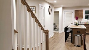 A modern kitchen with a central island, wooden flooring, and a staircase leading to another level.