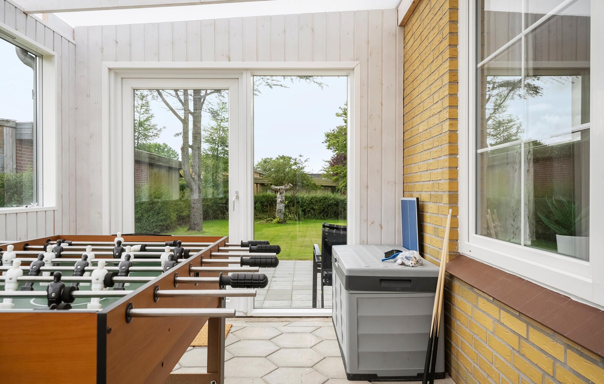 A room with a foosball table, a small table with items, and a window overlooking a garden.