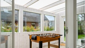 A sunlit room with a foosball table, large windows, and a view of a garden and a brick building. - Nice home in Skjern with WiFi (Skjern)