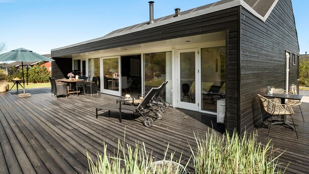A modern house with a deck, outdoor seating, and a large sliding glass door.