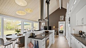 A modern kitchen with white cabinetry, a central island, and a large window overlooking a garden.