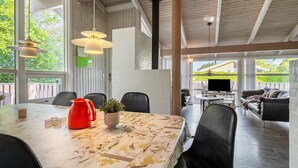 Ruime eethoek met een grote tafel, stoelen en een rode waterkoker. Er zijn hangende lampen en een uitzicht op de omgeving.