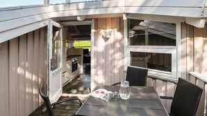 Een klein, afgesloten buitenkeuken met een tafel, stoelen, een raam en een deur die leidt naar een terras.