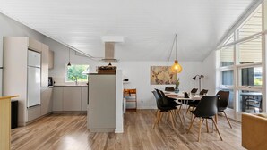 Cozinha moderna com ilha central, piso de madeira e área de jantar com cadeiras pretas e mesa.