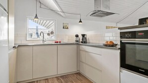 Uma cozinha moderna com armários brancos, forno embutido e janela com vista para um telhado com azulejos.
