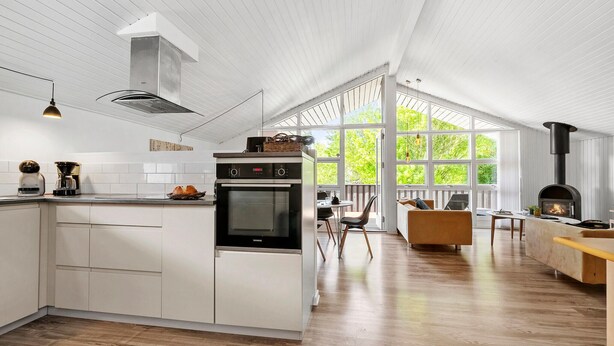 Uma cozinha moderna com armários brancos, forno embutido e uma grande janela com vista para o verde.