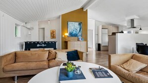 Uma sala de estar moderna com um conjunto de sofás, uma mesa de centro com objetos decorativos, uma mesa de pebolim e uma grande pintura abstrata na parede.