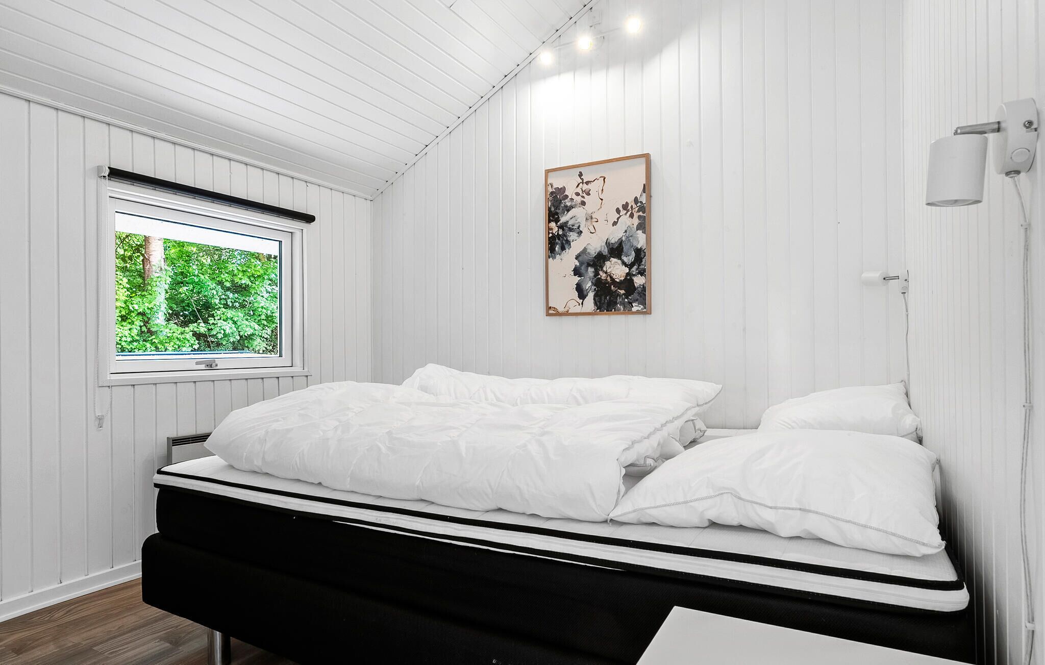 A bedroom with a bed, a window, and a wall-mounted light fixture.