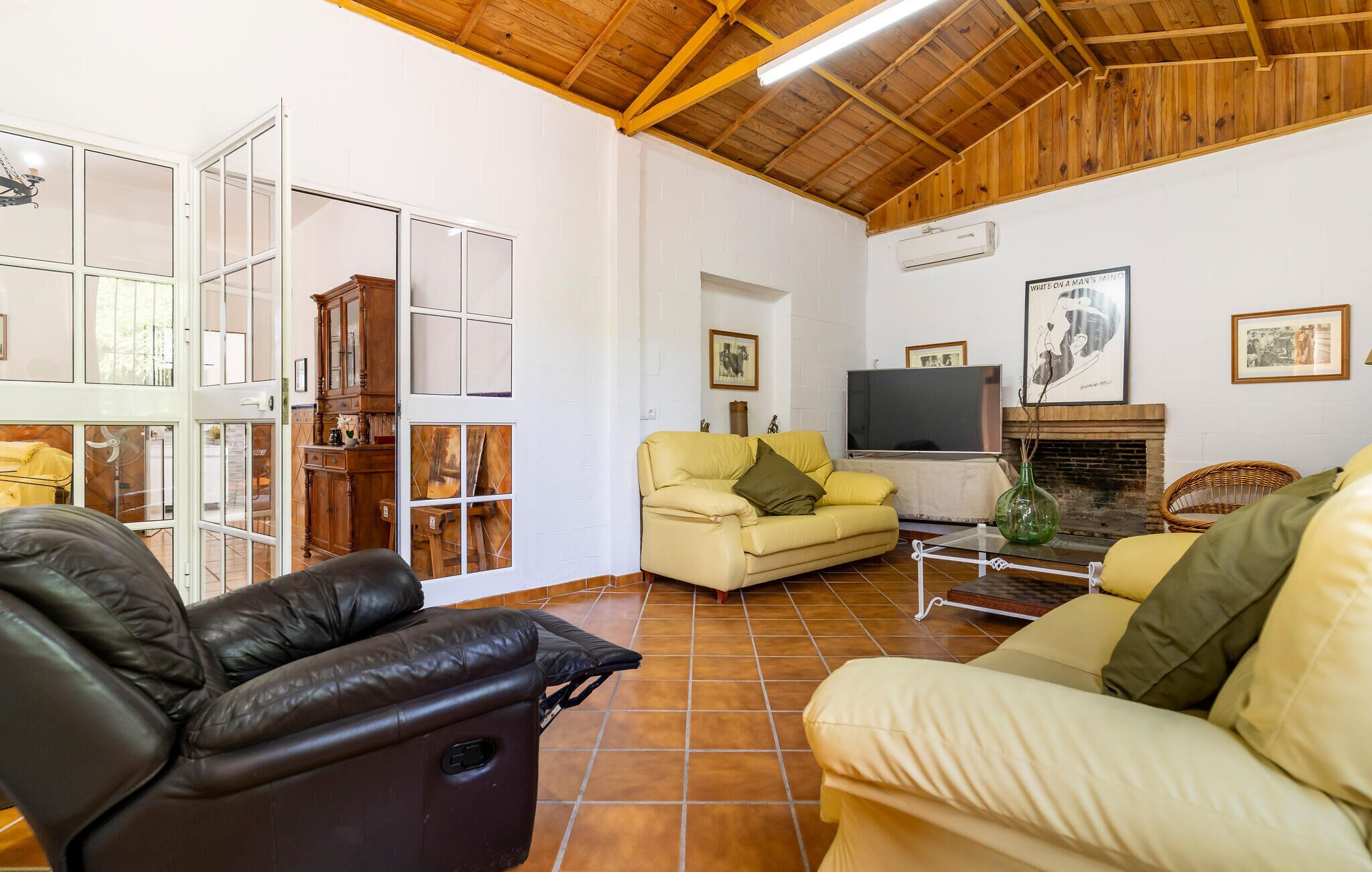 Amplia sala de estar con techo alto, chimenea, televisor y zona de comedor con mesa de vidrio.