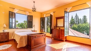 A bedroom with a bed, wooden dresser, nightstands, and a large window with curtains. - Pet friendly home in Guillena (Guillena)