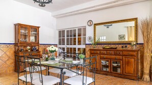 A dining area with a glass table, metal chairs, a wooden cabinet with glass doors, and a large mirror above the cabinet. - Pet friendly home in Guillena (Guillena)