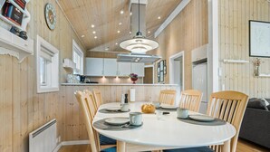 A modern kitchen with wooden paneling, a round dining table with chairs, and a built-in oven. - Nice home in Grevinge with WiFi (Grevinge)
