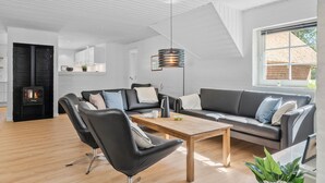 A modern living room with a black leather sofa, a wooden coffee table, and a black leather chair. There is a black fireplace with a white wall behind it, and a large window on the right side. - Nice home in Ulfborg with sauna (Ulfborg)