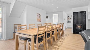 A modern dining area with a wooden table and chairs, a black leather sofa, and a stone fireplace. - Nice home in Ulfborg with sauna (Ulfborg)