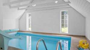 An indoor swimming pool with a blue slide, two windows, and a yellow inflatable toy on the right. - Nice home in Ulfborg with sauna (Ulfborg)