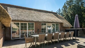 A thatched-roof building with a patio area featuring a table and chairs, a grill, and a covered umbrella. - Nice home in Ulfborg with sauna (Ulfborg)