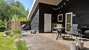 Eine Holzterrasse mit Gartenmöbeln, einer Tür und einem Fenster.