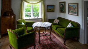 A room with a green sofa, two green armchairs, a wooden cabinet, a table with a white tablecloth, and a window with curtains. - 3 bedroom beautiful home in Stallarholmen (Stallarholmen)