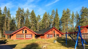 Une cabane à l’extérieur rouge, dotée de deux fenêtres et d’un toit noir, entourée d’une forêt.