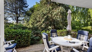Una terraza con una mesa redonda y sillas, rodeada de follaje y árboles.
