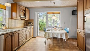 Una cocina con armarios de madera, una mesa de comedor con sillas y vista al exterior a través de una ventana.