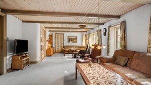 Un salón espacioso con techo de madera, televisor, sofá, mesa de centro y alfombra estampada.