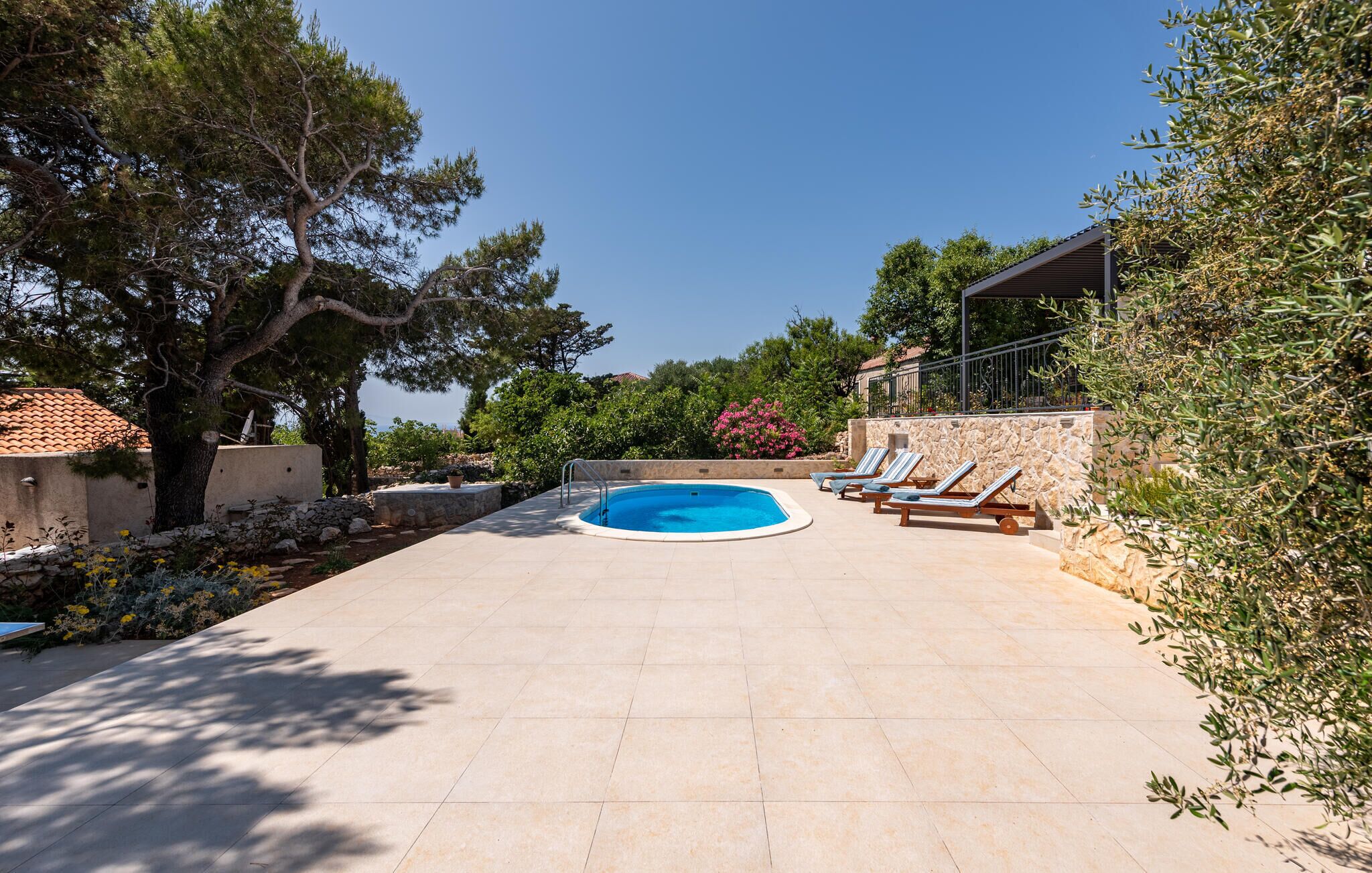 A swimming pool with lounge chairs, surrounded by stone walls and trees.