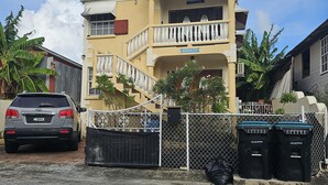 A two-story building with a balcony, a gated entrance, and a parked car. - Cozy home away from home apartment. (Bridgetown)