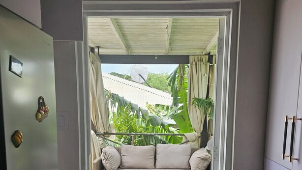 A doorway leading to a balcony with a sofa, a washing machine, and a tiled floor. - Cozy home away from home apartment. (Bridgetown)