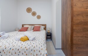 A neatly made bed with a patterned bedspread, pillows, and rolled towels. There is a bedside table with a lamp and a wall-mounted decorative item. - Lovely apartment in Povljana with WiFi (Povljana)
