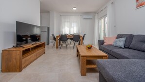 A modern living room with a flat-screen TV, wooden coffee table, grey sofa, and a dining area with chairs and a table. - Lovely apartment in Povljana with WiFi (Povljana)