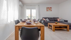A modern living room with a dining area, featuring a wooden table, chairs, a grey sofa, and a small coffee table. - Lovely apartment in Povljana with WiFi (Povljana)
