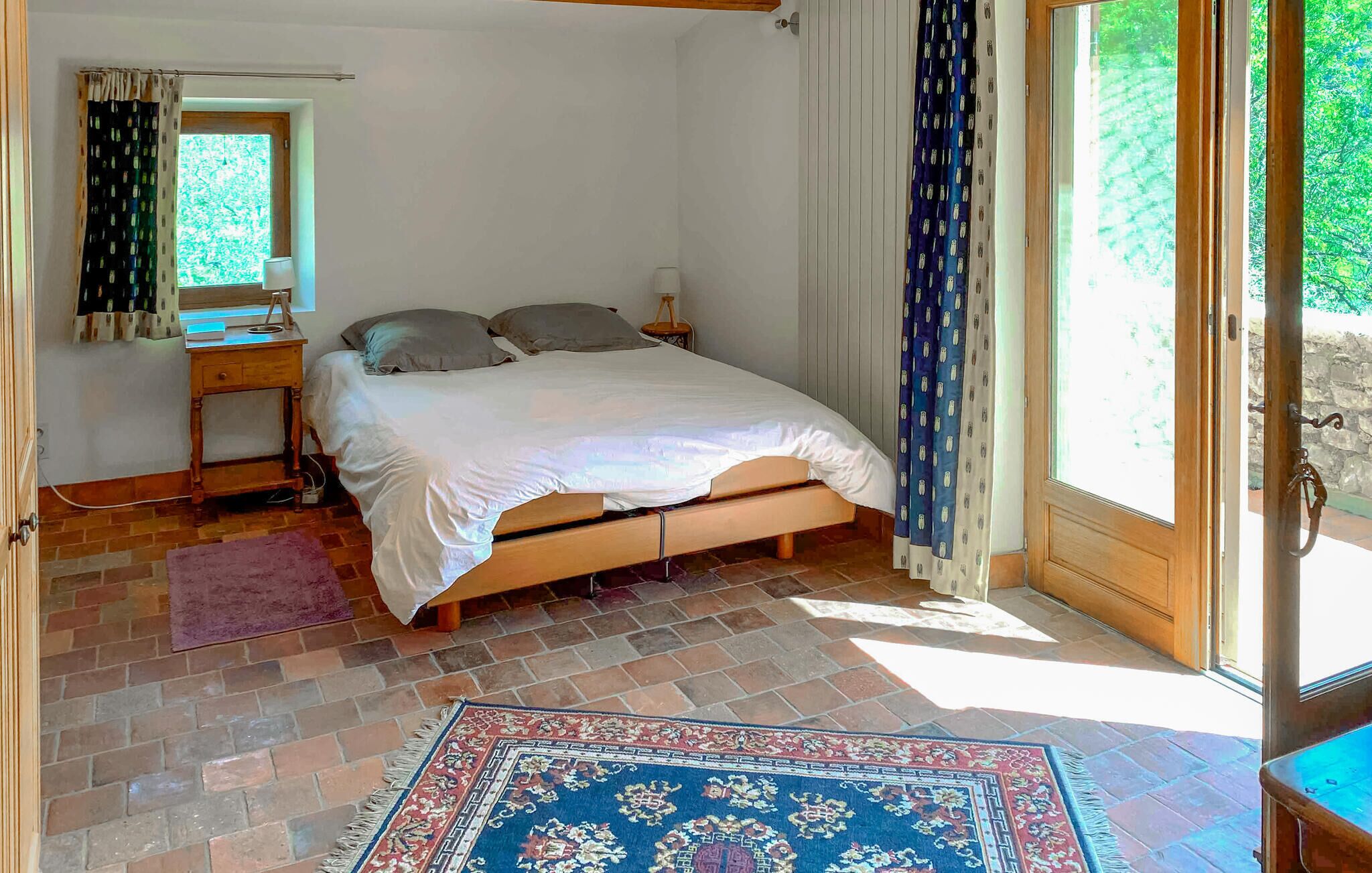 Una camera da letto con un letto, una scrivania, una sedia, una finestra con tende e vista sul verde.