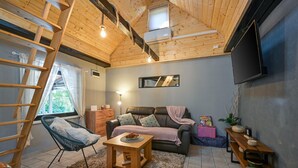Ein gemütliches Wohnzimmer mit Holzboden, einer Couch, einem Couchtisch und einem an der Wand befestigten Fernseher.