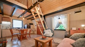 Ein gemütliches Interieur mit Holzbalkendecke, einer Küchenzeile, einem Esstisch mit Stühlen, einer Couch und einem Fenster mit Vorhängen.