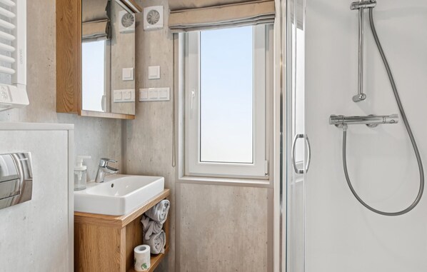 Un baño moderno con cabina de ducha de vidrio, tocador de madera y un ventanal grande.