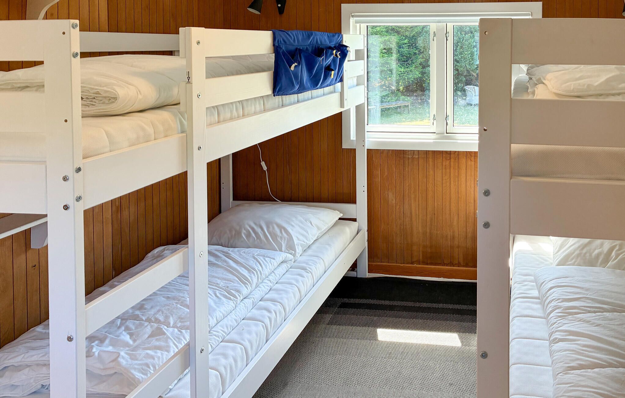 A bunk bed room with wooden walls, a window, and a view of greenery outside.