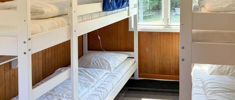 A bunk bed room with wooden walls, a window, and a view of greenery outside.
