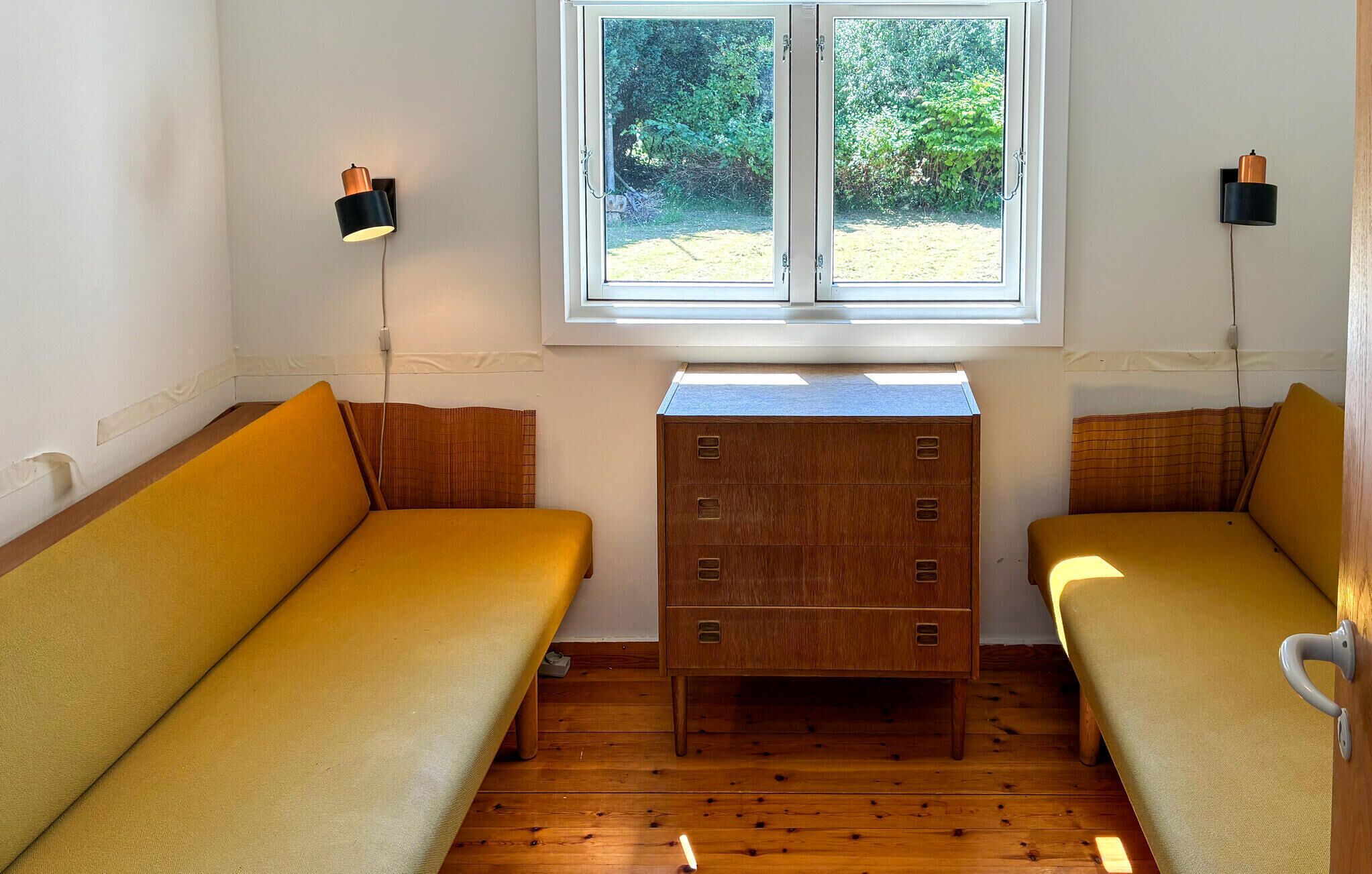 Een kamer met twee gele banken, een houten dressoir en twee wandlampen.