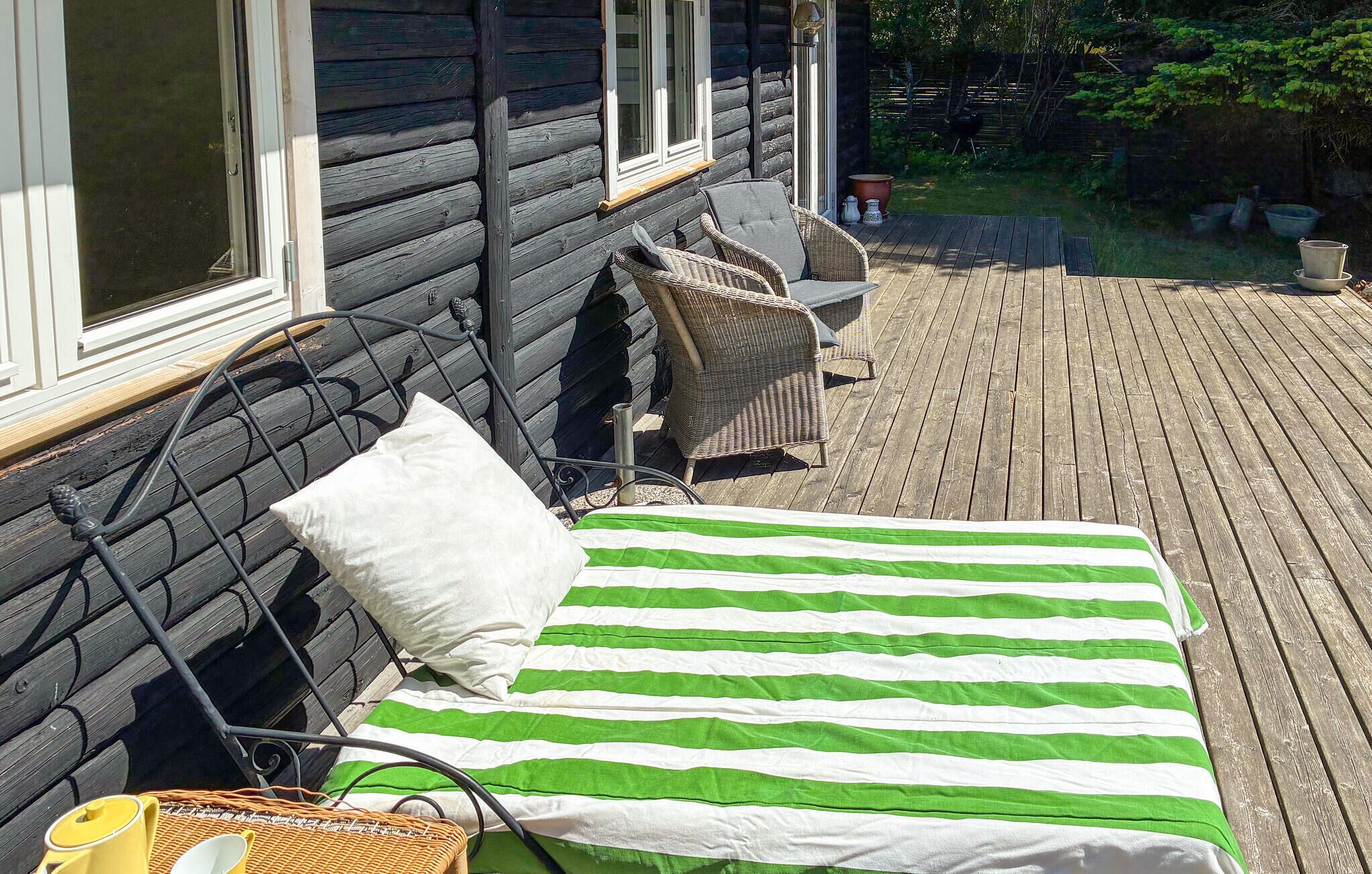 A bed with green and white striped bedding, a white pillow, and a wicker chair on a wooden deck.