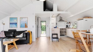 Ein geräumiger Wohnbereich mit schwarzem Ledersofa, Esstisch aus Holz und einer Küche mit weißen Schränken und einem eingebauten Backofen.