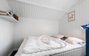 A bedroom with a white bed, a blue lamp, and a framed picture on the wall.