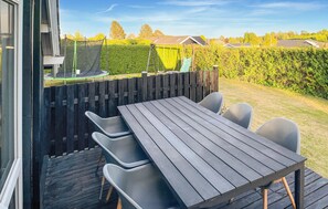 An outdoor patio with a wooden table and chairs, a trampoline, and a wooden fence.