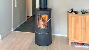 Una sala de estar moderna con un estufa de leña negra, un mueble de madera y piso de baldosas.