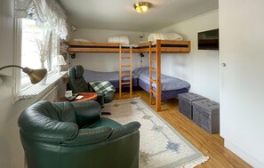Een kleine kamer met een stapelbed, een bureau met lamp, een leren fauteuil en een klein poufje.