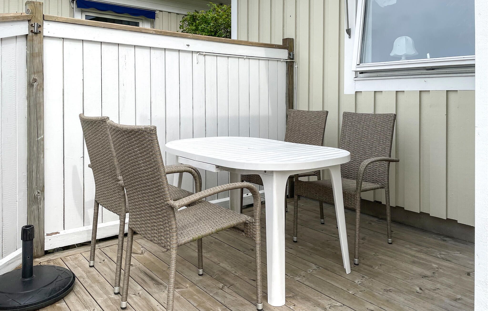 A patio with a white table and wicker chairs, a wooden deck, and a white fence.