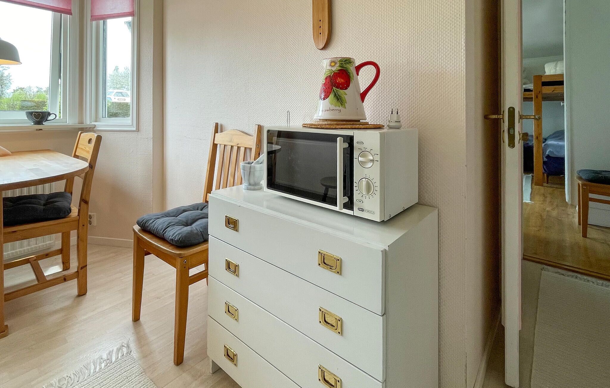 A kitchen with a microwave on a cabinet, a chair, a table, and a window with a view outside.