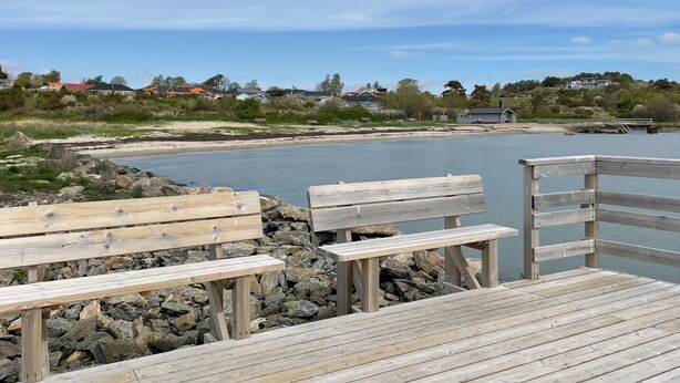 A wooden pier with benches overlooking a calm body of water, with houses and greenery in the background. - 1 bedroom gorgeous home in åsa (Åsa)