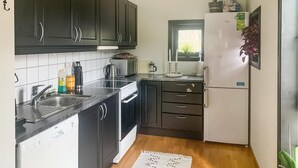 Una cocina compacta con armarios oscuros, un refrigerador blanco, una cafetera y un lavamanos.