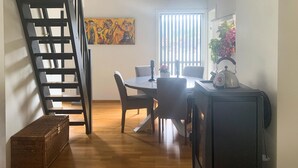 Un comedor con una mesa, sillas, un refrigerador, una cesta y un cuadro en la pared.